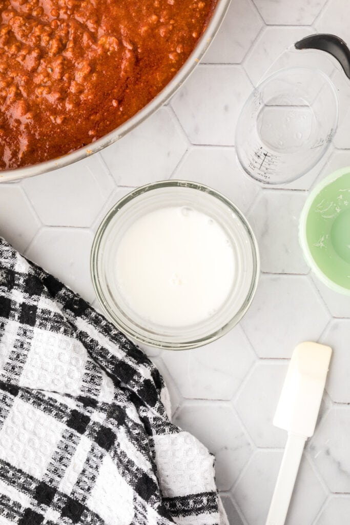 Cornstarch slurry in a small glass bowl beside a skillet of Chili Cheese Burrito filling.