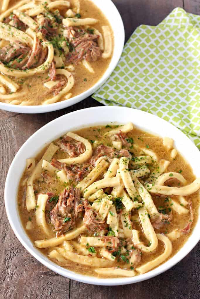 Two bowls of homemade beef and noodles with shredded roast, thick egg noodles, and parsley