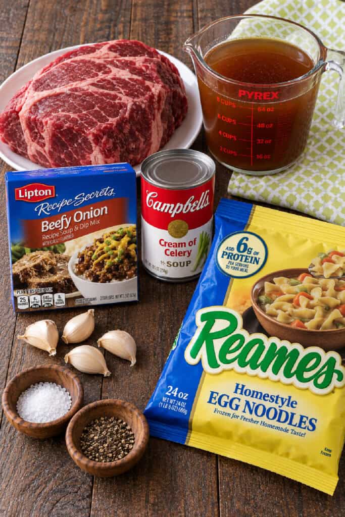 Ingredients for slow cooker beef and noodles including beef roast, broth, egg noodles, soup mix, cream soup, garlic, salt, and pepper