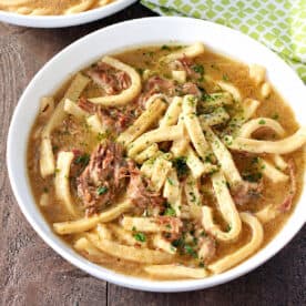 Bowl of beef and noodles with tender shredded roast, thick noodles, and parsley in beef broth