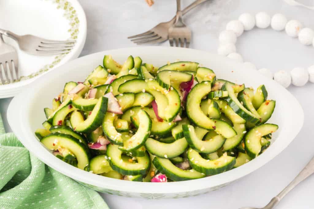 cucumber salad served in a bowl with sliced cucumbers, sesame seeds, and red onion pieces