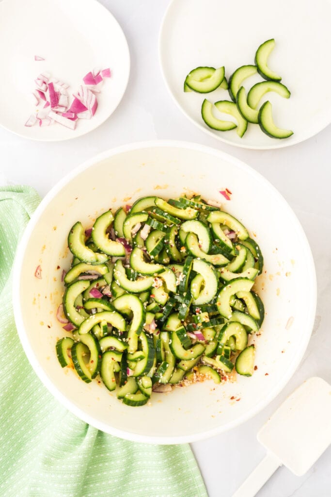 cucumber salad being mixed in a bowl with sesame seeds, red onion, and dressing