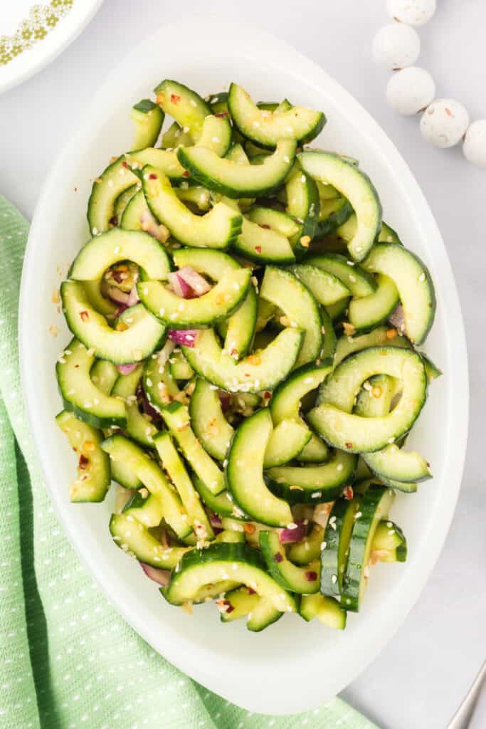 finished cucumber salad in a serving dish with sesame seeds, red onion, and dressing visible