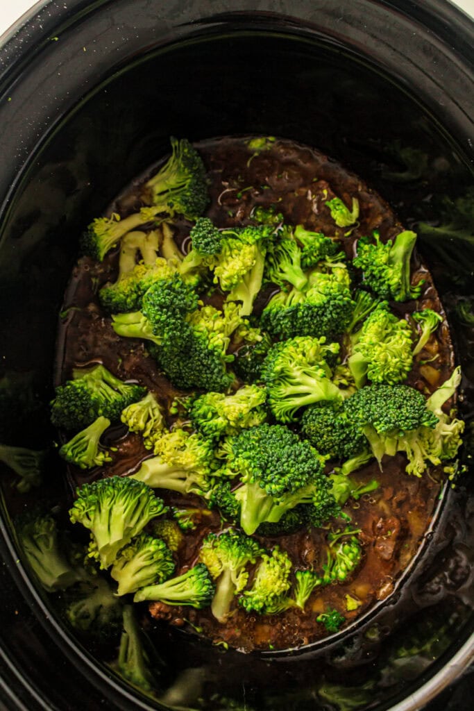 Fresh broccoli florets added to cooked beef mixture in a slow cooker