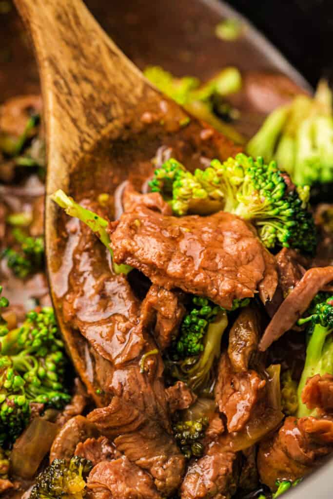 Close up of beef and broccoli in sauce with a wooden spoon
