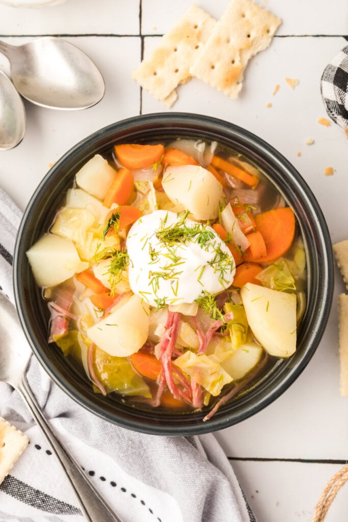 looking down into a bowl of corned beef and cabbage soup garnished with sour cream and dill