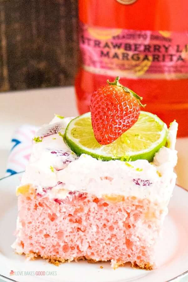 Boozy Strawberry Margarita Poke Cake on a plate with fresh fruit.