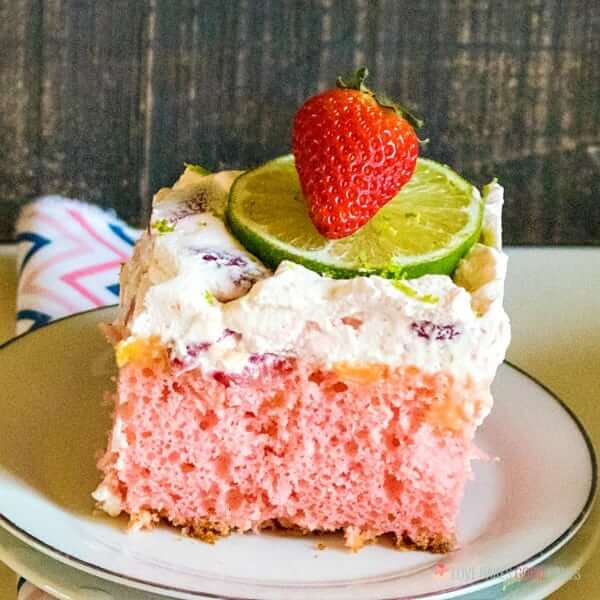 Boozy Strawberry Margarita Poke Cake on a plate with fresh fruit close up.
