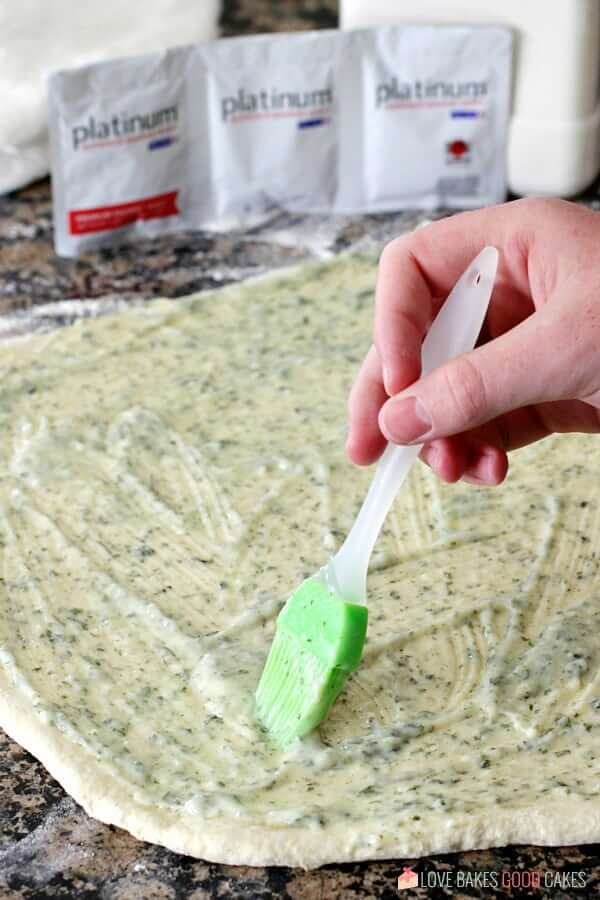 Cheesy Garlic Bread "Cinnamon" Roll dough being basted with butter sauce.