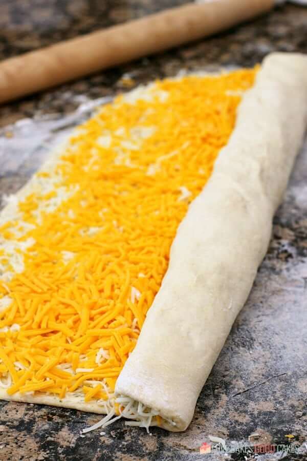 Cheesy Garlic Bread "Cinnamon" Roll dough with shredded cheese being rolled up.