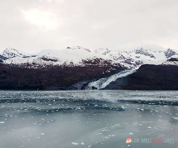 5 Benefits of a Balcony Room on a Cruise - An iceberg sits in a body of water with mountains in the background.