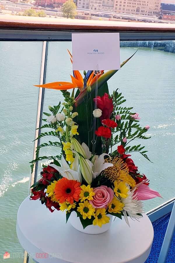 A flower arrangement with a card sitting on a table overlooking the harbor from a cruise ship.