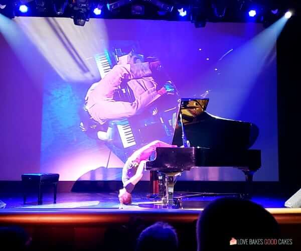 A man playing a piano upside down on stage in the theater of a cruise ship.