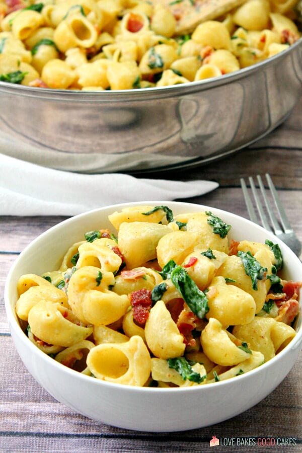 One Pot Creamy Bacon Spinach Pasta in a skillet and in a white bowl with a fork.