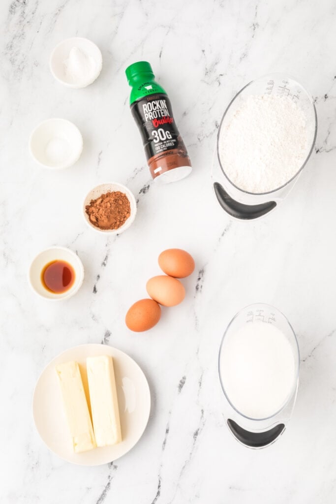 Ingredients needed to make Chocolate Milk Cake Recipe, including chocolate milk, cake flour, butter, eggs, cocoa powder, and vanilla
