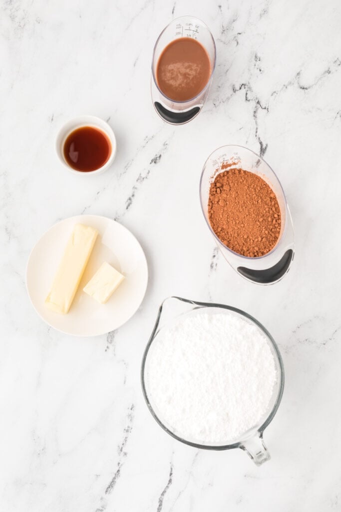 Ingredients for homemade chocolate buttercream frosting, including butter, powdered sugar, cocoa powder, vanilla, and chocolate milk