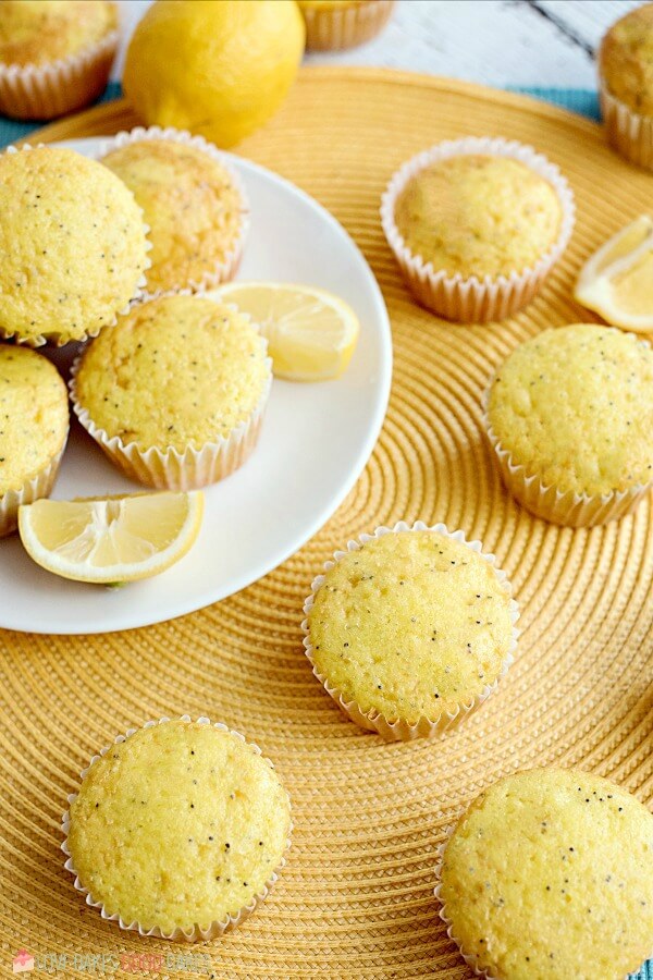 Lemon Poppy Seed Muffins piled up on a white plate with fresh lemon slices.