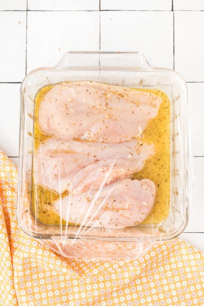 Chicken breasts marinating in the dish covered with plastic wrap