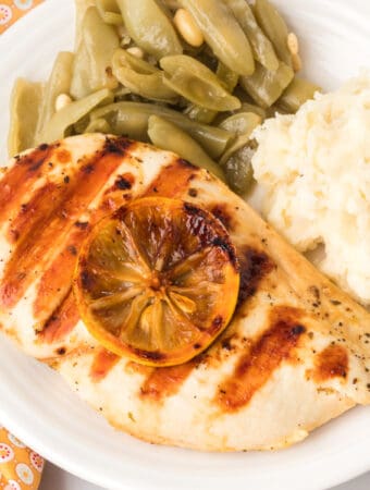 Square-cropped image of grilled chicken breast with grill marks and lemon slice, served with mashed potatoes and green beans