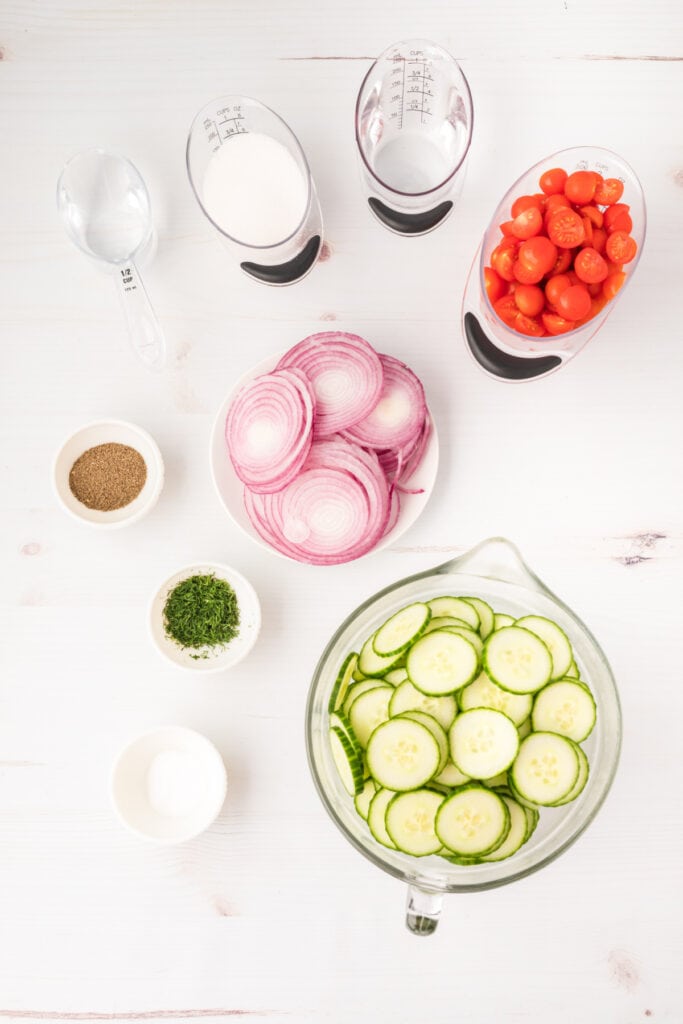 Overhead shot of salad ingredients in bowls, including cucumbers, tomatoes, red onions, dill, and vinegar