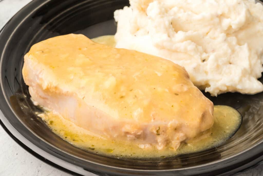 Close-up of slow cooker pork chop topped with rich golden gravy beside mashed potatoes.