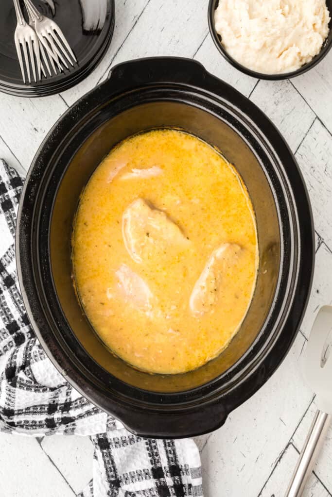 Cooked pork chops simmering in creamy gravy inside a slow cooker, ready to serve.