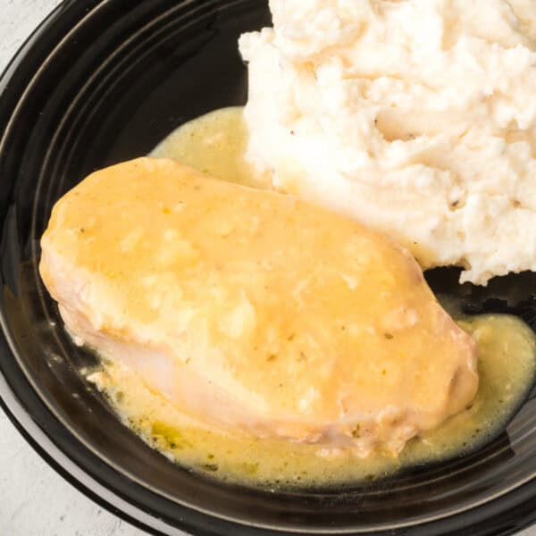 Square crop of a creamy slow cooker pork chop served with mashed potatoes on a black plate.