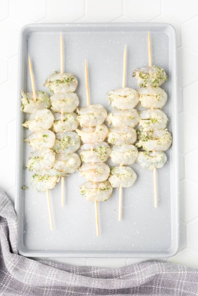 Raw shrimp skewered and arranged on a gray tray, seasoned and ready to grill.