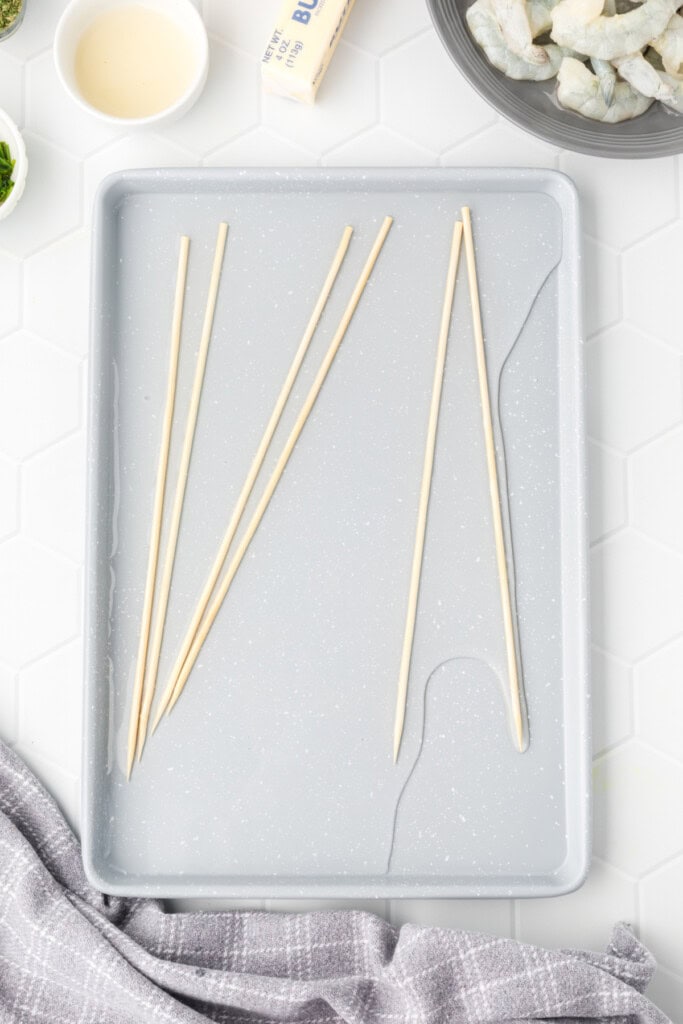 Wooden skewers soaking in water on a gray tray.