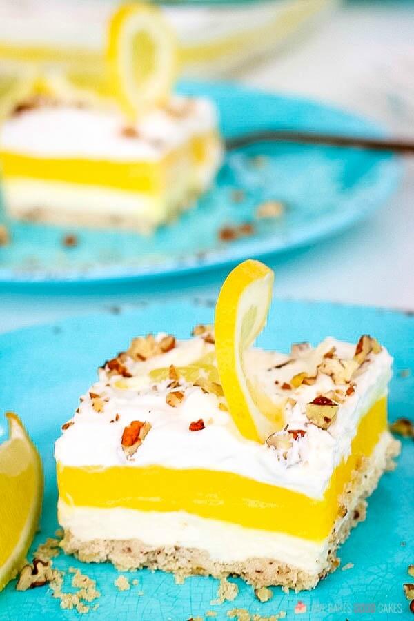 This Lemon Lush Delight is a cool, creamy, lemony dessert that's sure to be a new favorite! It's perfect any time you want a sunny citrus treat! A close up of a piece of lemon lush delight pie on blue plates.
