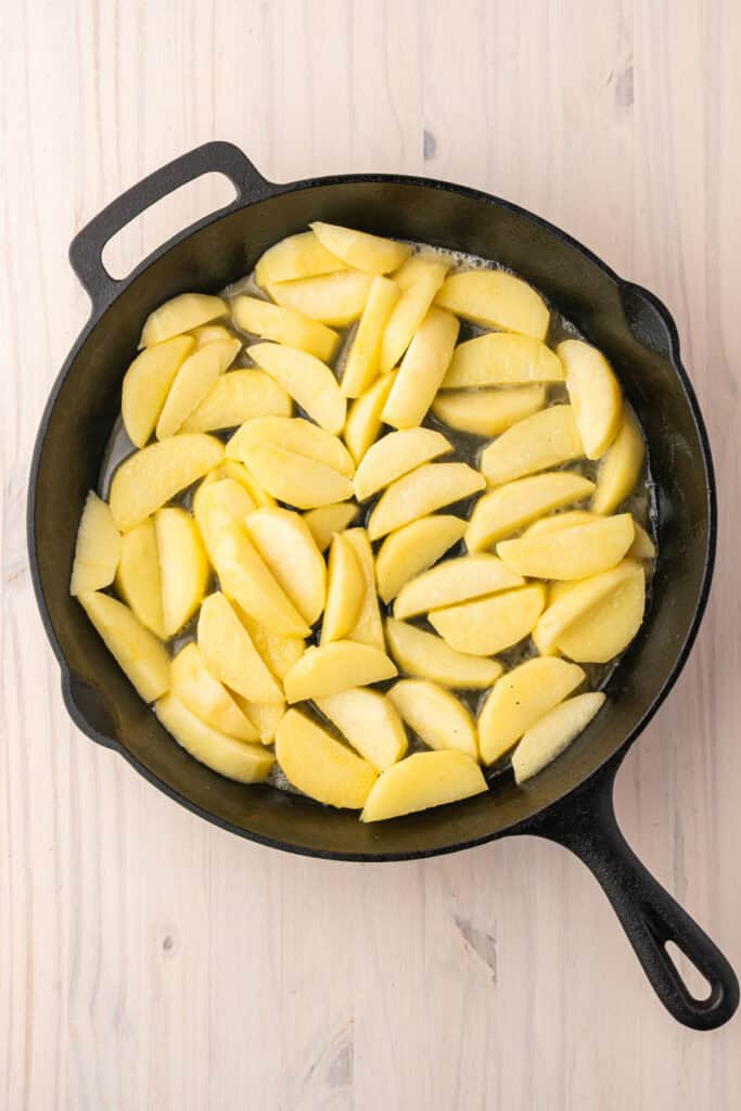 Fresh apple slices cooking in melted butter in a cast iron skillet.