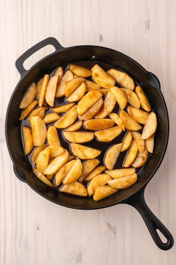 Apples simmering with cinnamon, brown sugar, and spices in a skillet.