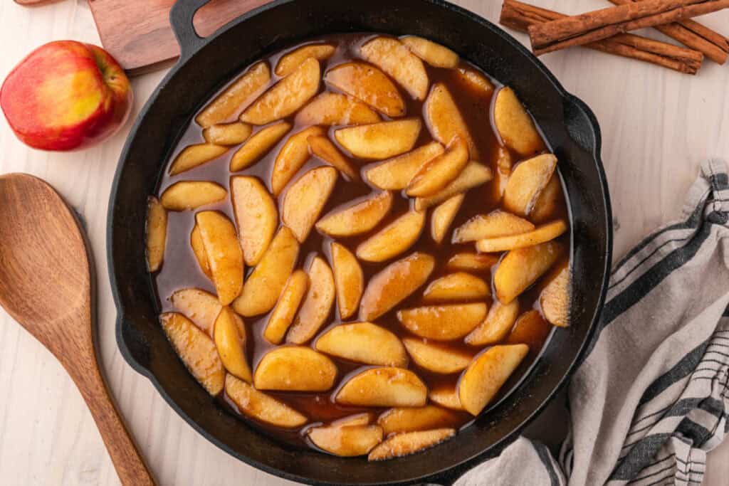 Homemade Southern Fried Apples in a cast iron skillet with fresh apples and cinnamon sticks.