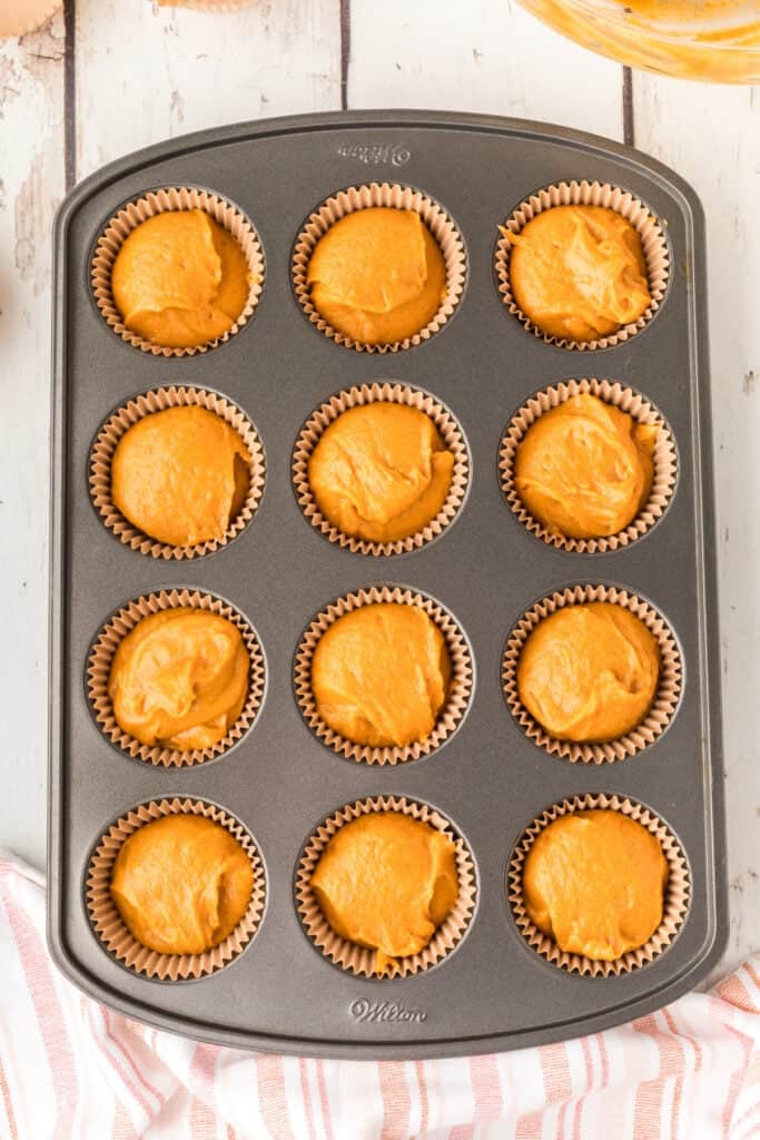 Pumpkin batter scooped evenly into lined muffin tin cups, ready for baking