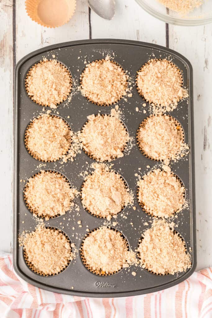 Muffin tin filled with batter, each topped generously with crumb mixture before baking