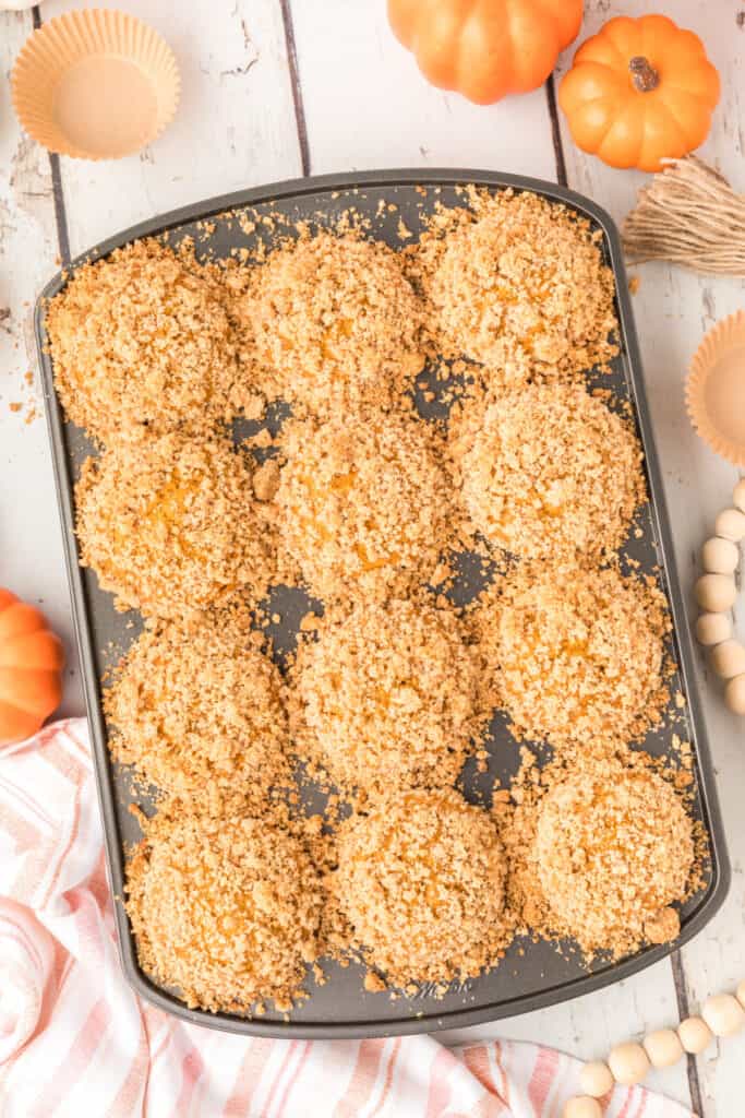 Freshly baked muffins in the tin, covered with golden crumb topping and surrounded by fall decor
