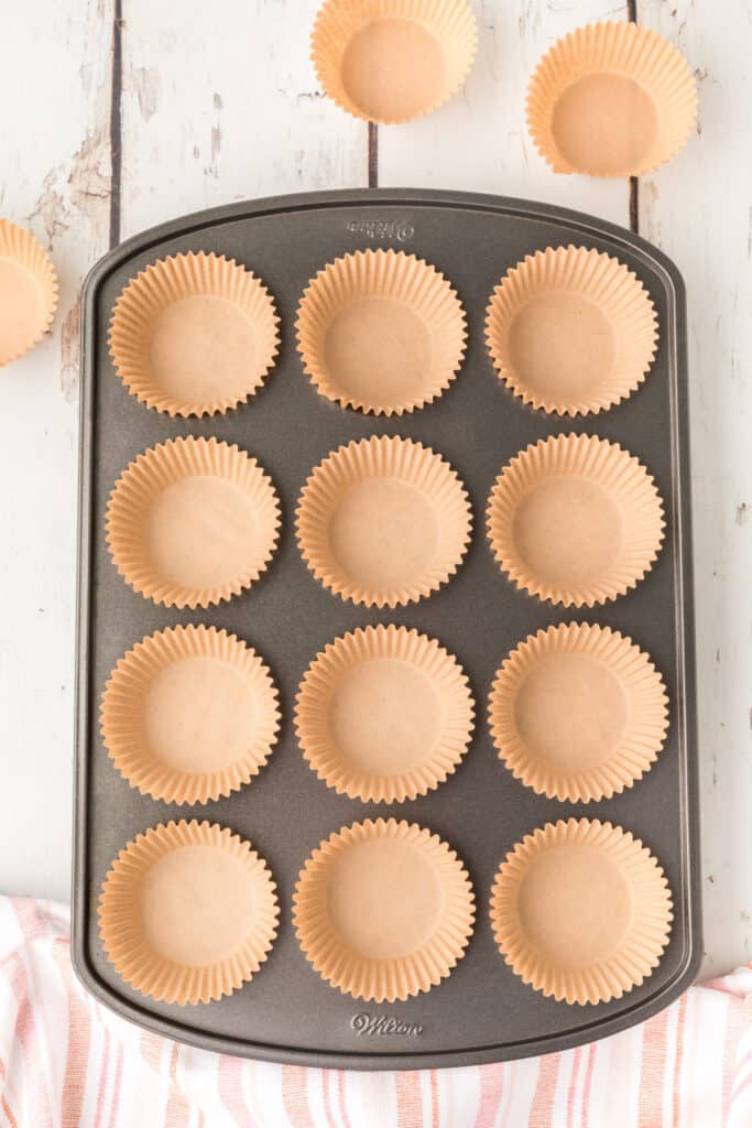 Empty muffin pan lined with brown paper cupcake liners on a rustic white background