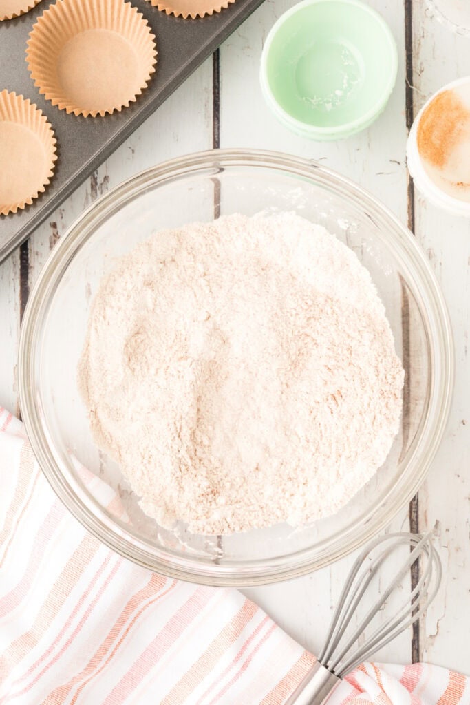 Whisked dry ingredients fully combined in a glass mixing bowl beside the muffin pan
