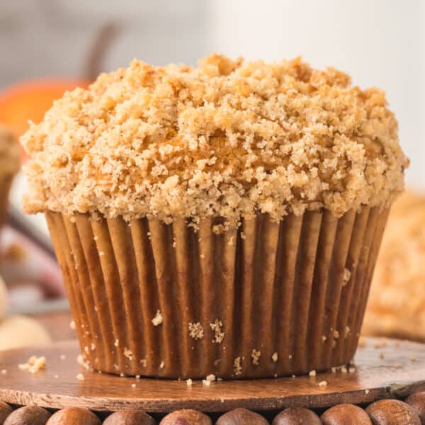 Square crop of a crumb topped muffin on a wooden pedestal with soft background fall decor