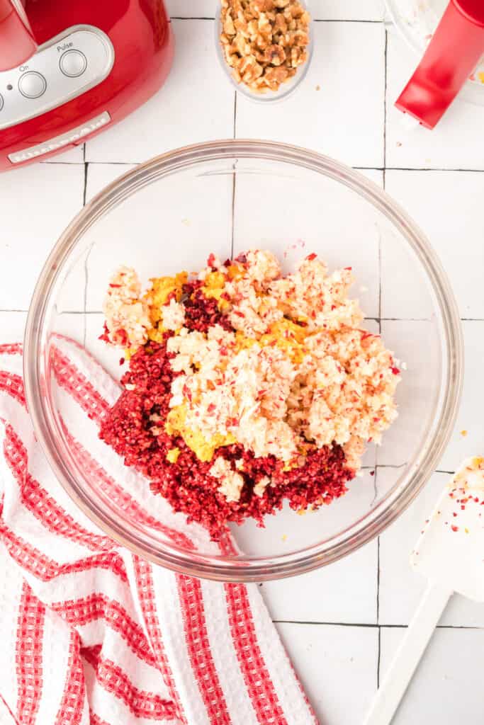 Mixing bowl filled with chopped cranberries, oranges, and apples, ready for walnuts and sugar to be added to complete the relish mixture.