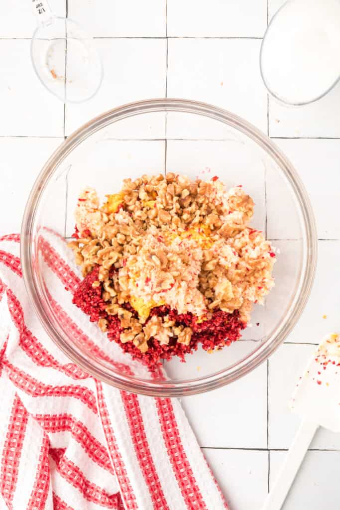 Mixing bowl with chopped cranberries, oranges, apples, and chopped walnuts layered on top, ready to be stirred together.