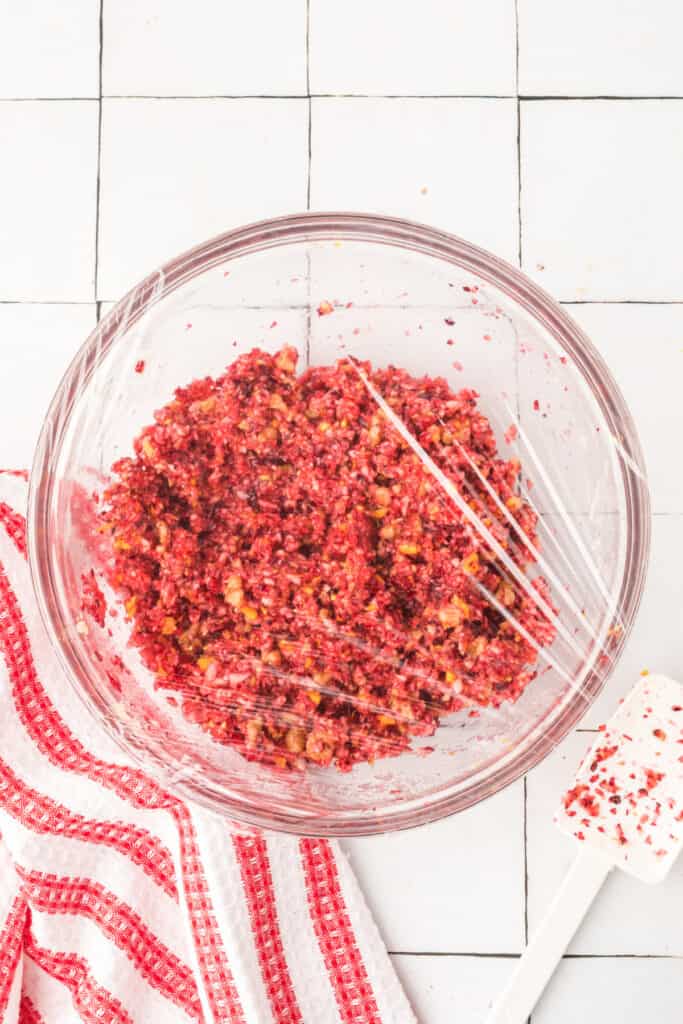 Freshly made cranberry relish covered with plastic wrap and ready to chill in the refrigerator.