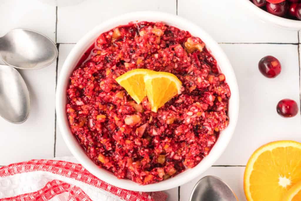 Overhead shot of finished cranberry relish served in a white bowl, topped with orange slices and surrounded by fresh cranberries.