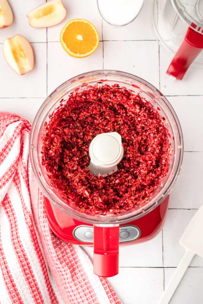 Finely chopped orange pieces inside the red food processor, showing a bright yellow-orange mixture.
