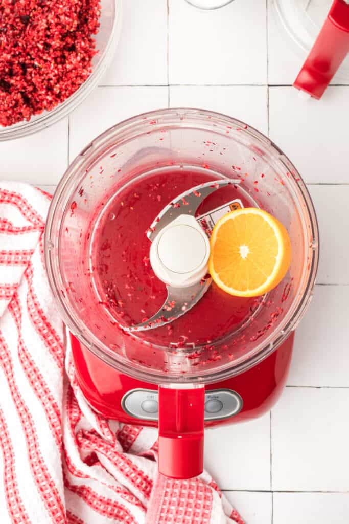 Finely chopped orange pieces inside the red food processor, showing a bright yellow-orange mixture.