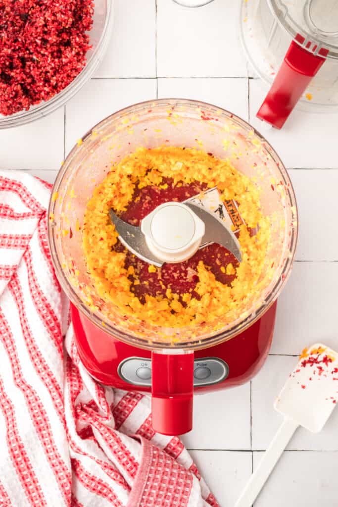 Finely chopped orange pieces inside the red food processor, showing a bright yellow-orange mixture.
