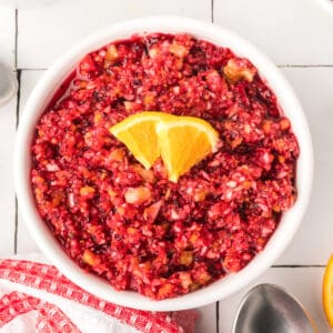 Overhead square image of cranberry relish in a white bowl topped with orange slices, showcasing its vibrant red color and fresh texture.