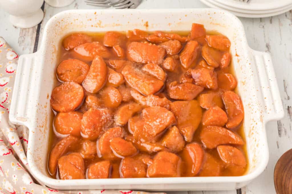 Homemade candied yams in a baking dish surrounded by plates and serving utensils
