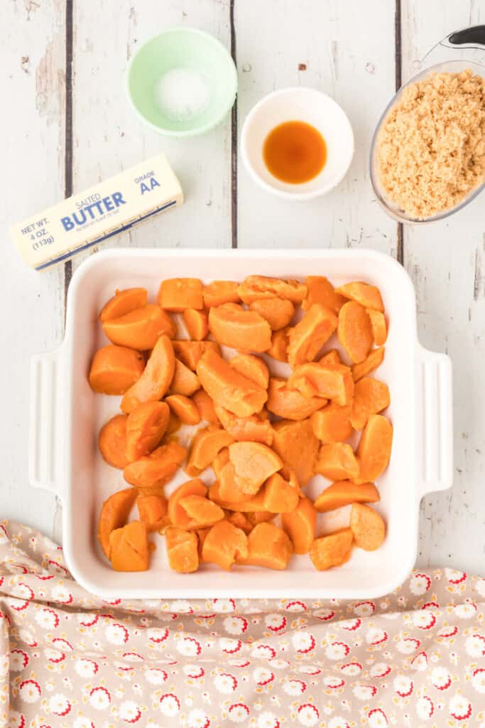 Drained canned yams in a baking dish with brown sugar, butter, vanilla, and salt nearby