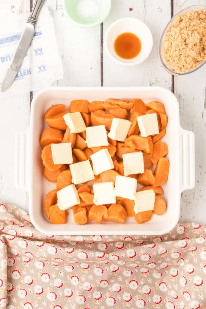 Pieces of butter scattered over canned yams in a white baking dish